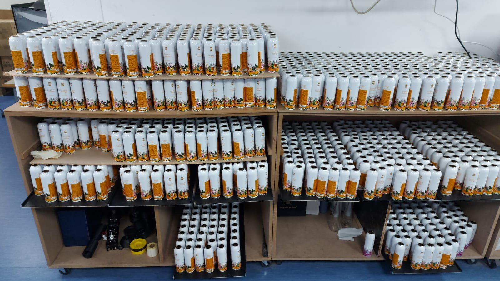 Rows of printed Ajmal Tropical Mango body spray cans racked on trolleys at the studio after printing