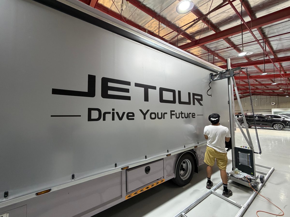 طابعة wallPen عند طرف المشمّع بعد طباعة JETOUR وعبارة Drive Your Future، وبجانبها فنّي