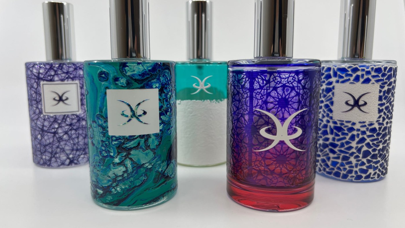 Five glass perfume bottles printed with different full wrap designs, each carrying a logo knocked out in opaque white