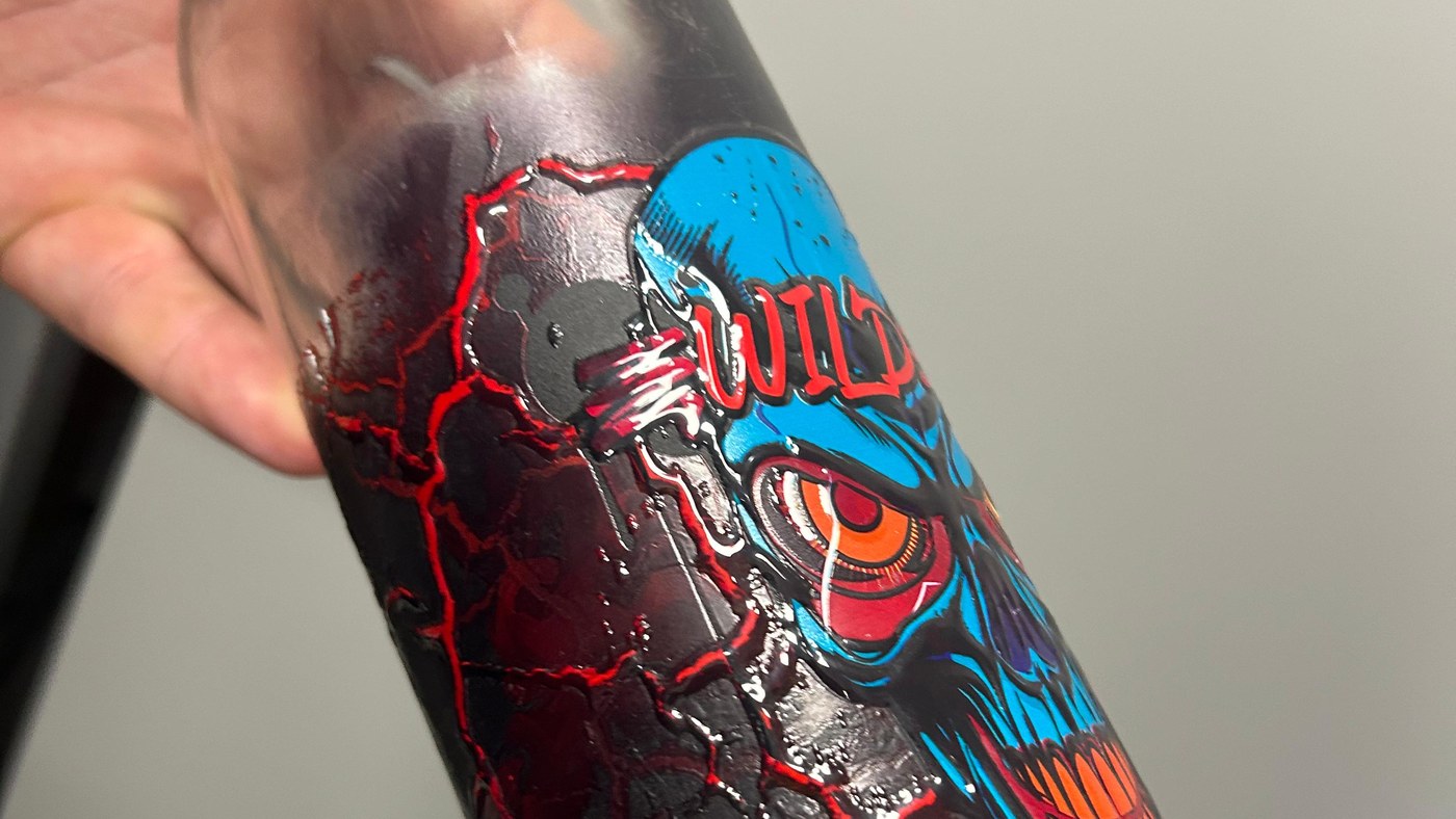 Close detail of a clear glass bottle printed with a raised varnish design, the red cracked pattern standing proud of the surface