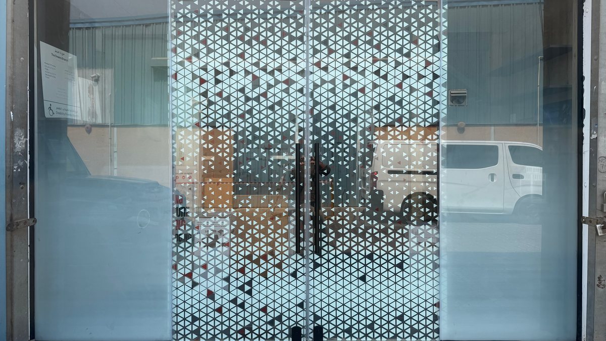 A bi-parting sliding glass door printed with a dense triangle pattern, between two fixed glass panels that fade from clear at the top to solid white towards the floor