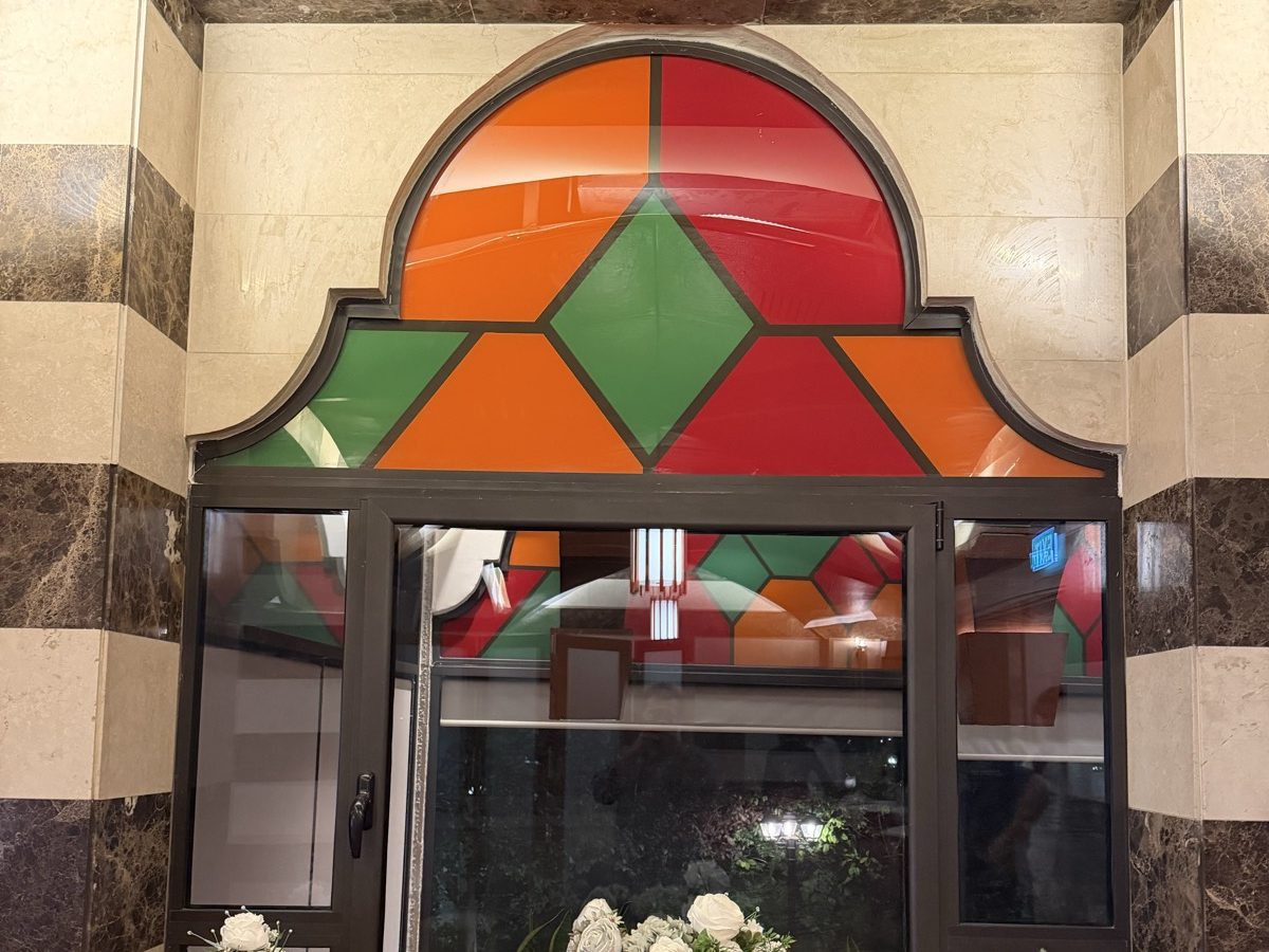 An ogee-arched printed glass panel in red, green and orange above a marble window niche