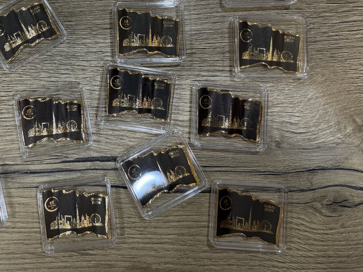 Solid gold commemorative pieces printed with a black ground, the Dubai skyline left as bare metal, each sealed in a clear capsule