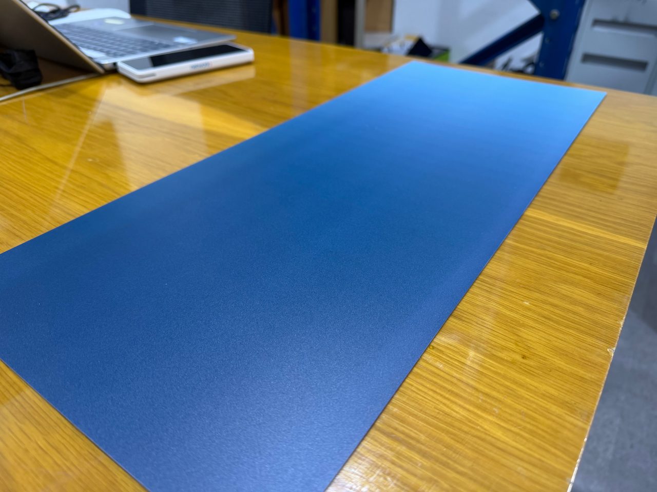 A gradient-printed aluminium panel on a workbench seen at a low angle, the blue fading evenly from light to deep navy