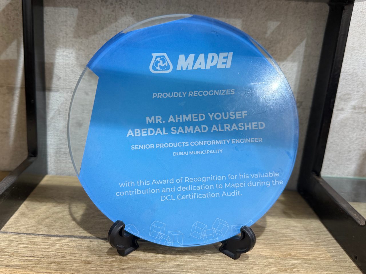 A round glass recognition plaque printed with a blue flood and white lettering