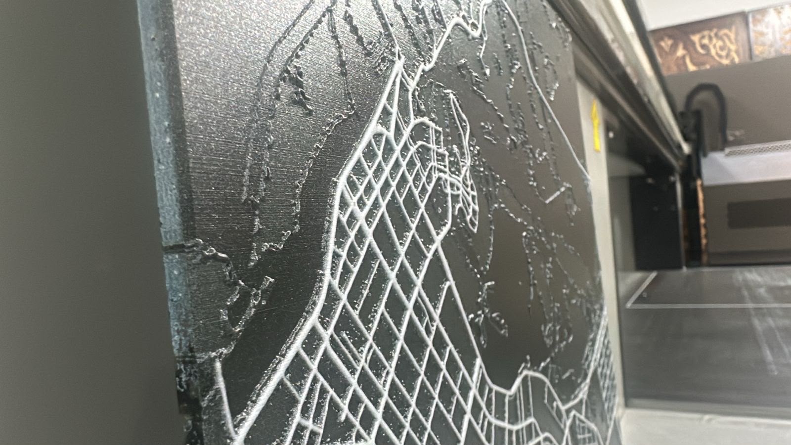 A raised white line drawing printed on a dark panel, the cured ink standing proud of the surface