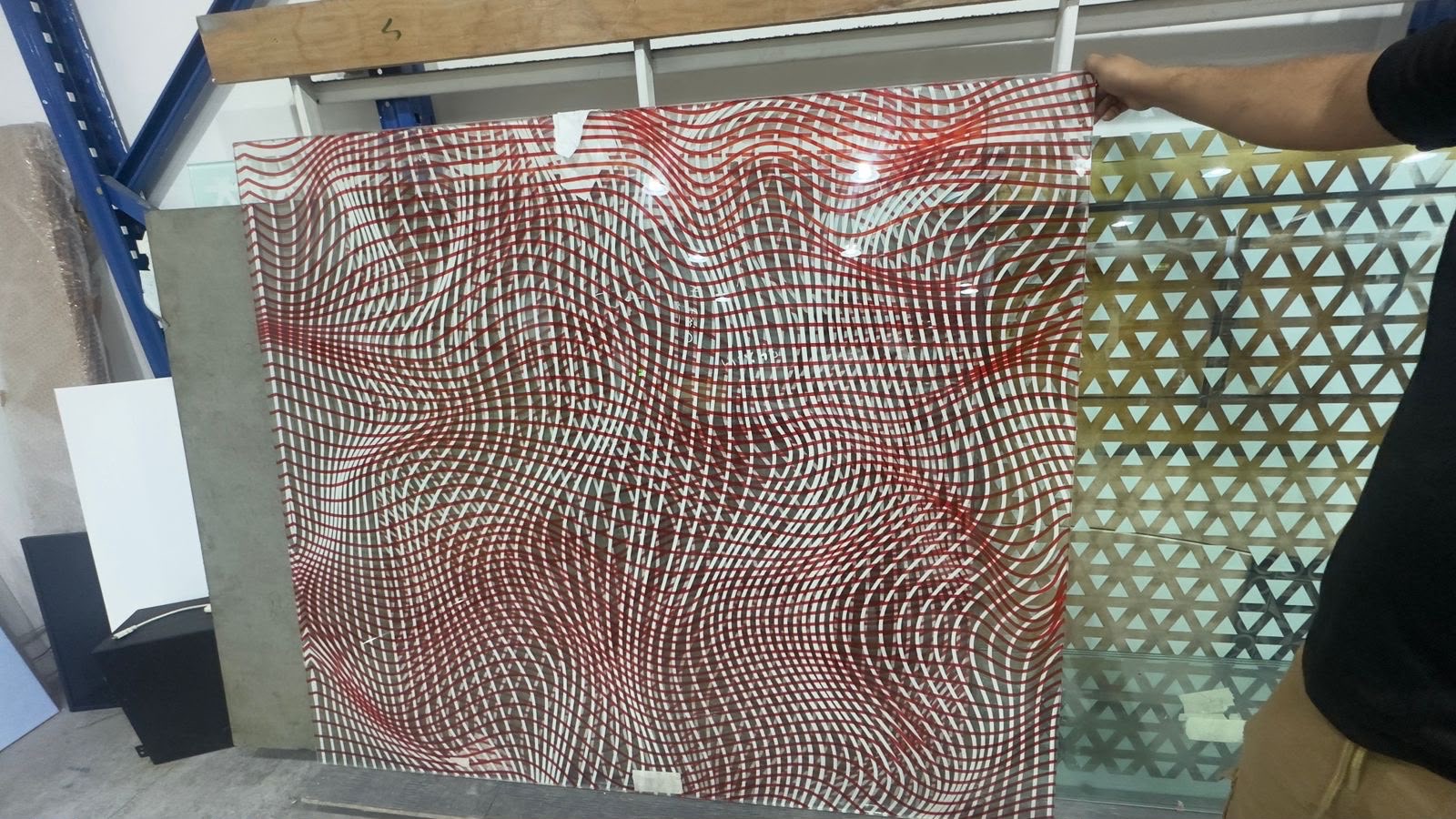 A large glass panel printed with a red woven pattern, held in the workshop