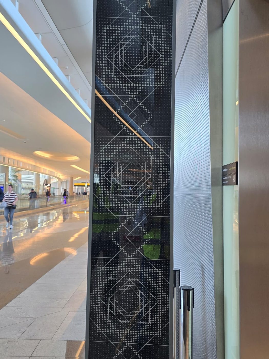 A mall column clad in dark glass printed with a geometric pattern of dotted lines