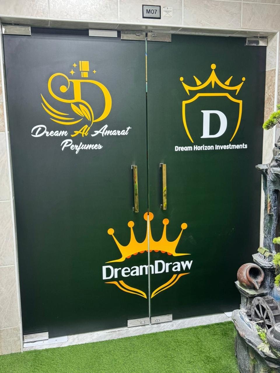 Entrance doors printed with the Dream Al Amarat Perfumes, Dream Horizon Investments and DreamDraw marks in gold on dark glass