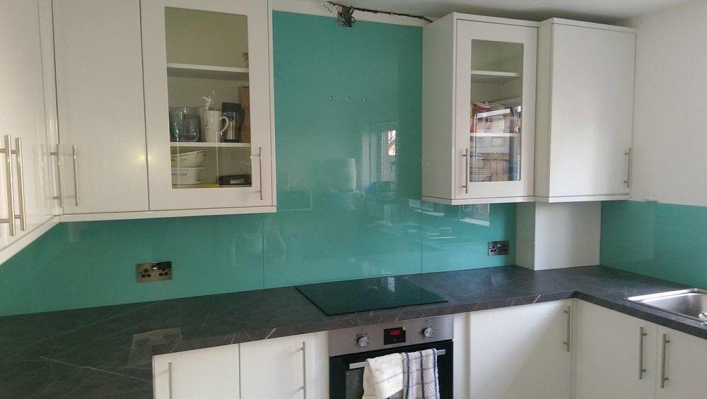 A bright green splashback returning around a corner between wall and base units