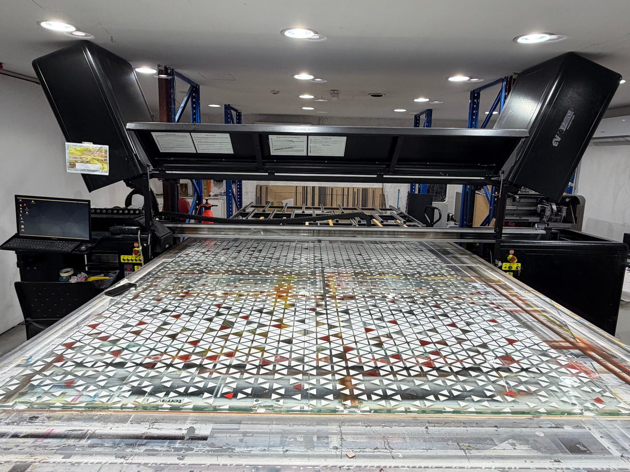 Large clear glass panels laid across the bed of a UV flatbed printer, printed with a lattice of white and red triangles
