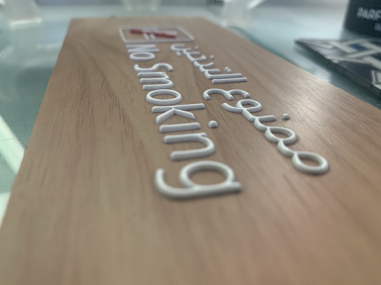 Bilingual English and Arabic no-smoking signage printed in raised white ink on a wood-grain panel