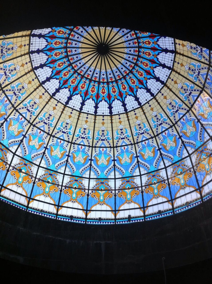 An ornamental stained-glass style ceiling dome in blue, gold and red, lit from above