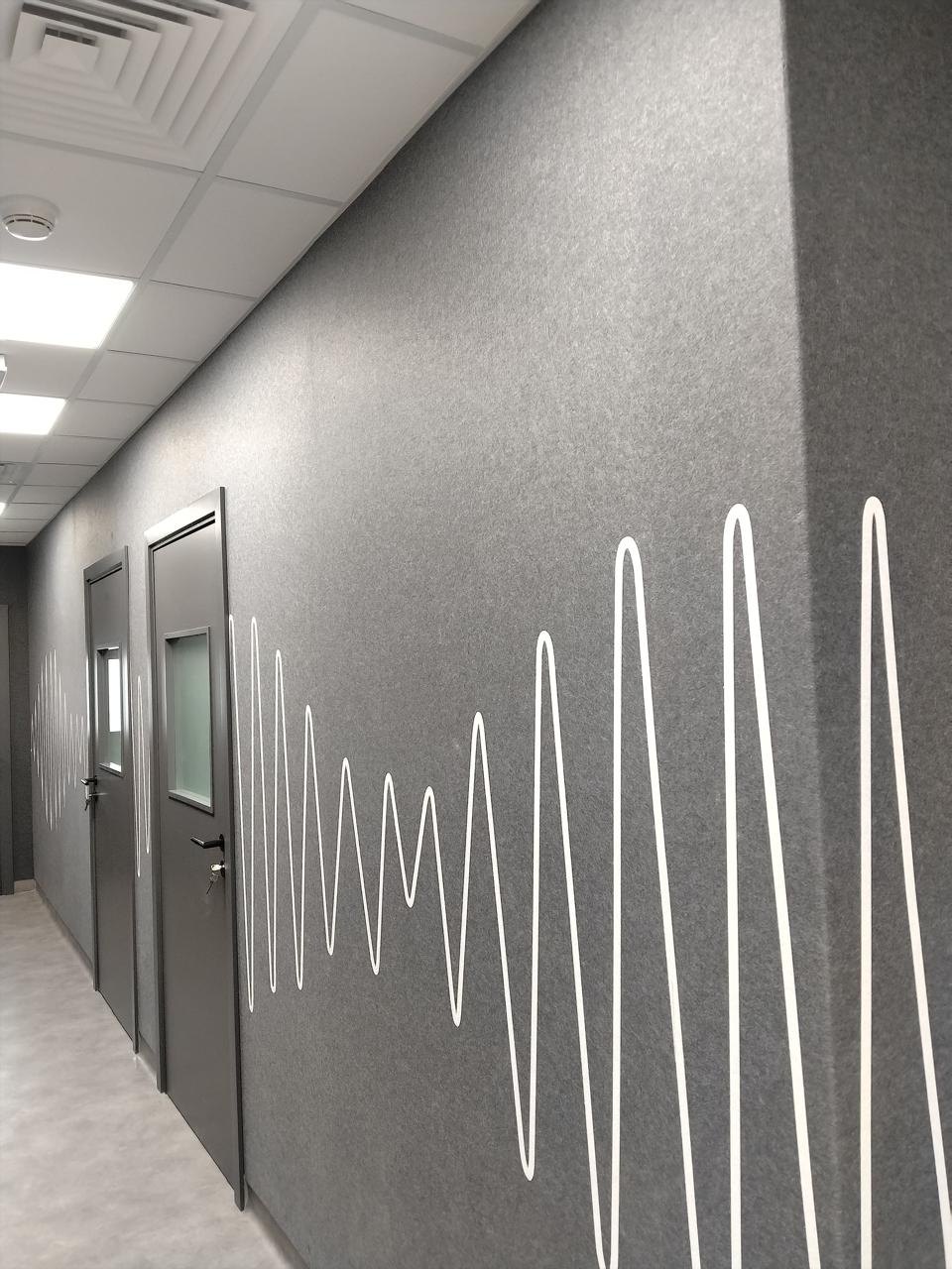 A corridor lined with grey felt acoustic wall panels, a white sound wave line printed across the panels and around a corner