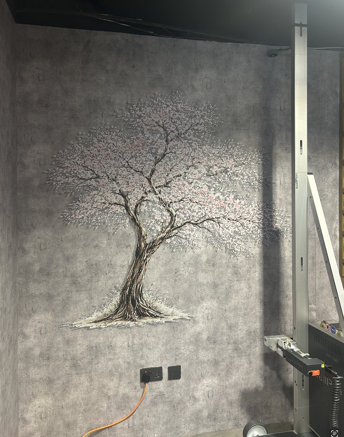 A blossom tree printed directly onto a dark textured grey wall, with the wall printer standing on the floor beside it