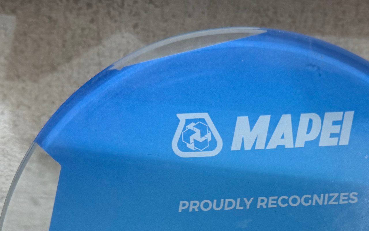 Close-up of a rounded clear plaque printed solid blue, with the MAPEI logo and Proudly Recognizes in white and a clear unprinted edge