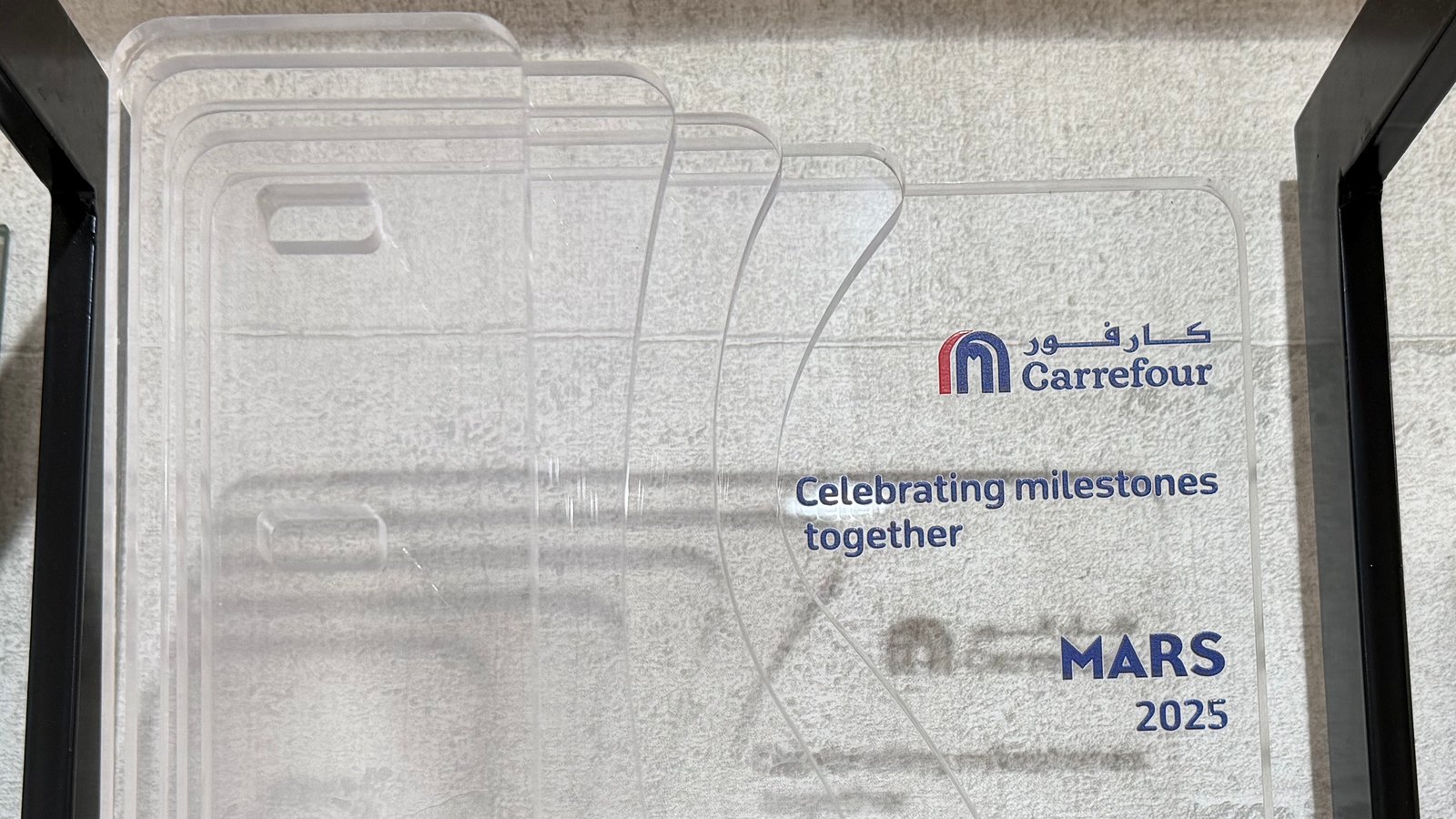 Clear acrylic award sheets fanned in a row, one printed in blue and red with a logo in Arabic and English, a message and a date