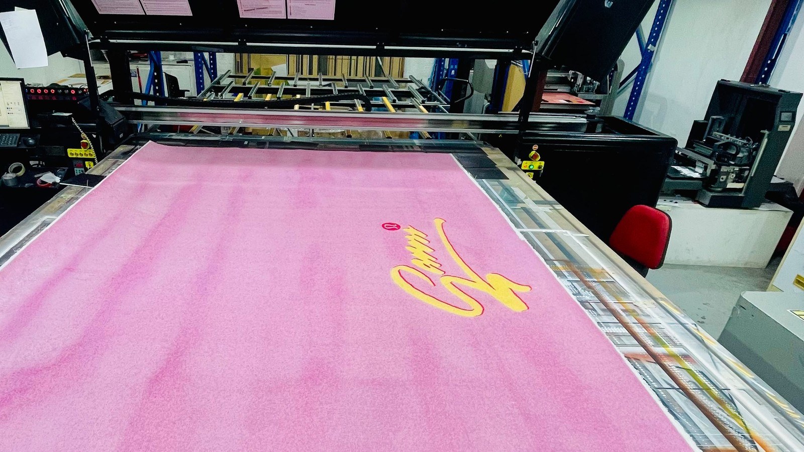 A rug printed light pink from end to end with a yellow script and the red Lululemon logo, lying on the belt of the IQDEMY EVO 2500 flatbed at Sun Studio in Al Quoz, Dubai