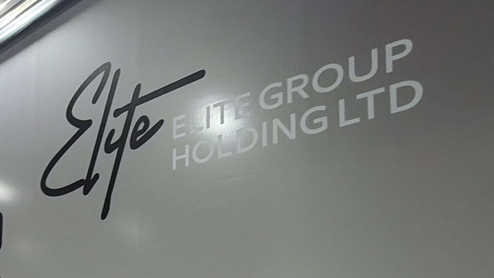 Close-up of the truck tarpaulin: the Elite script printed in black and ELITE GROUP HOLDING LTD printed in white ink on the grey coating