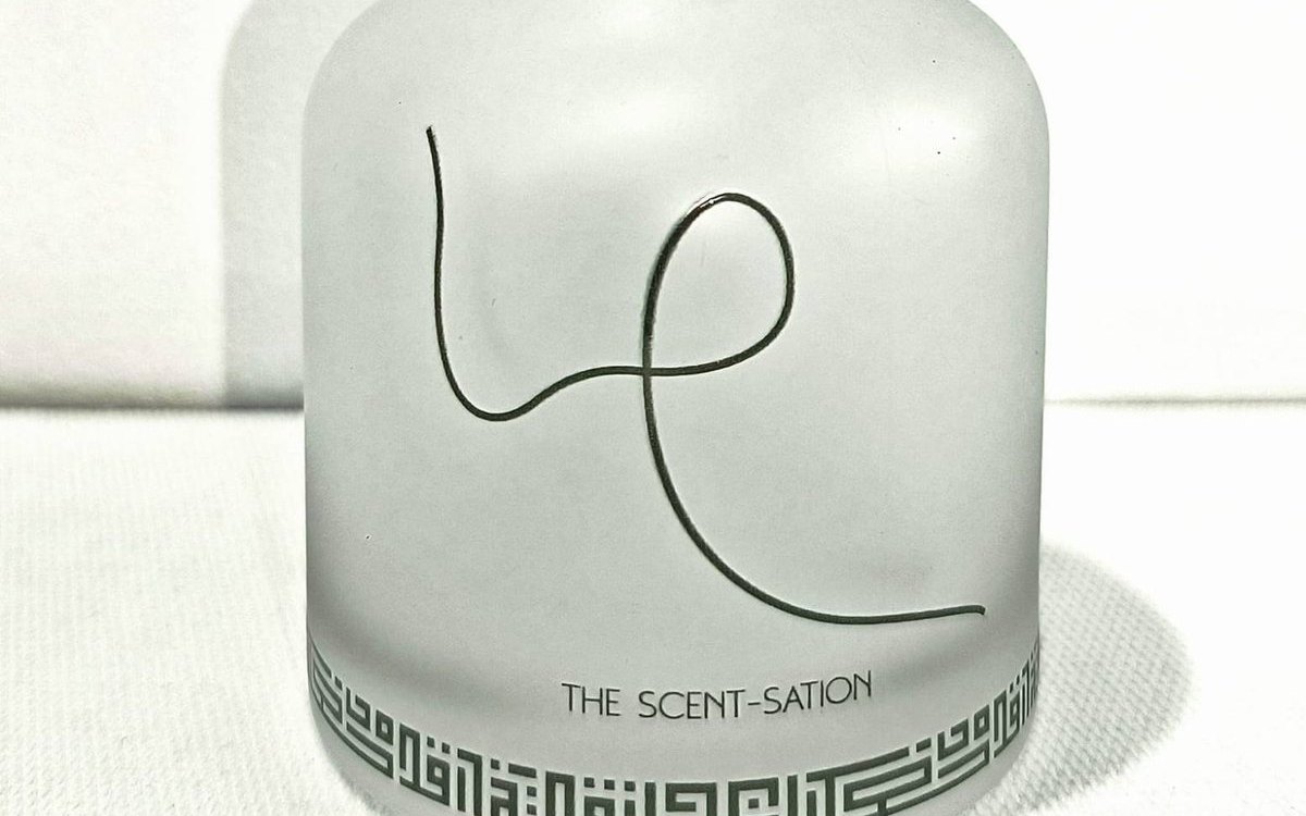 Detail of a frosted glass diffuser bottle printed in one dark colour with a signature line and a Kufic-style geometric band