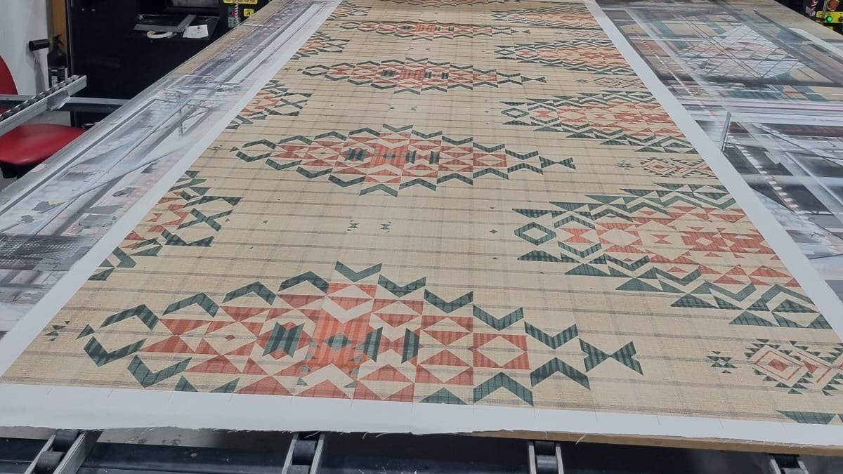 A kilim-style geometric pattern in terracotta and green printed on a finished flat-woven rug on the belt of a UV flatbed