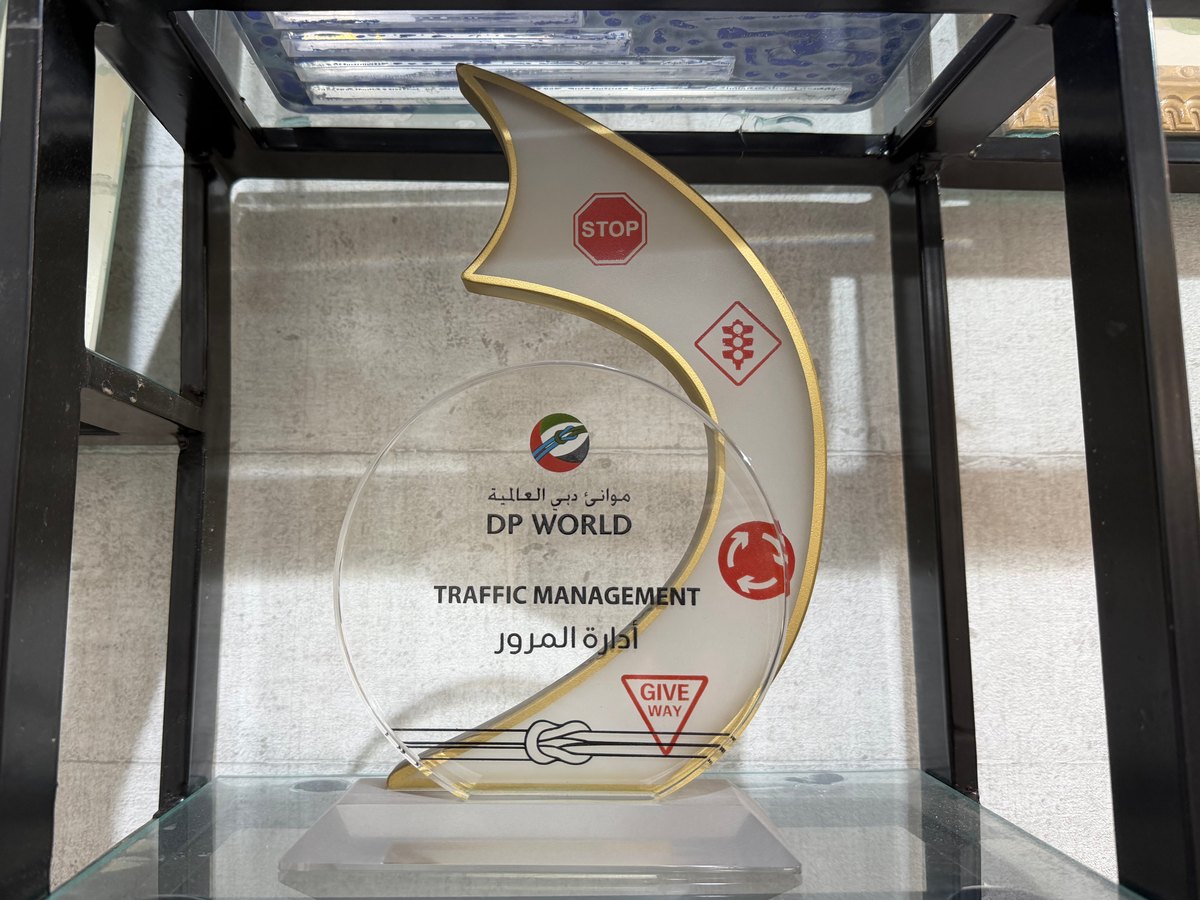 A layered acrylic award on a frosted base: a clear disc printed with a colour logo and a title in English and Arabic, in front of a white wave with red road-sign symbols and a gold-coloured edge