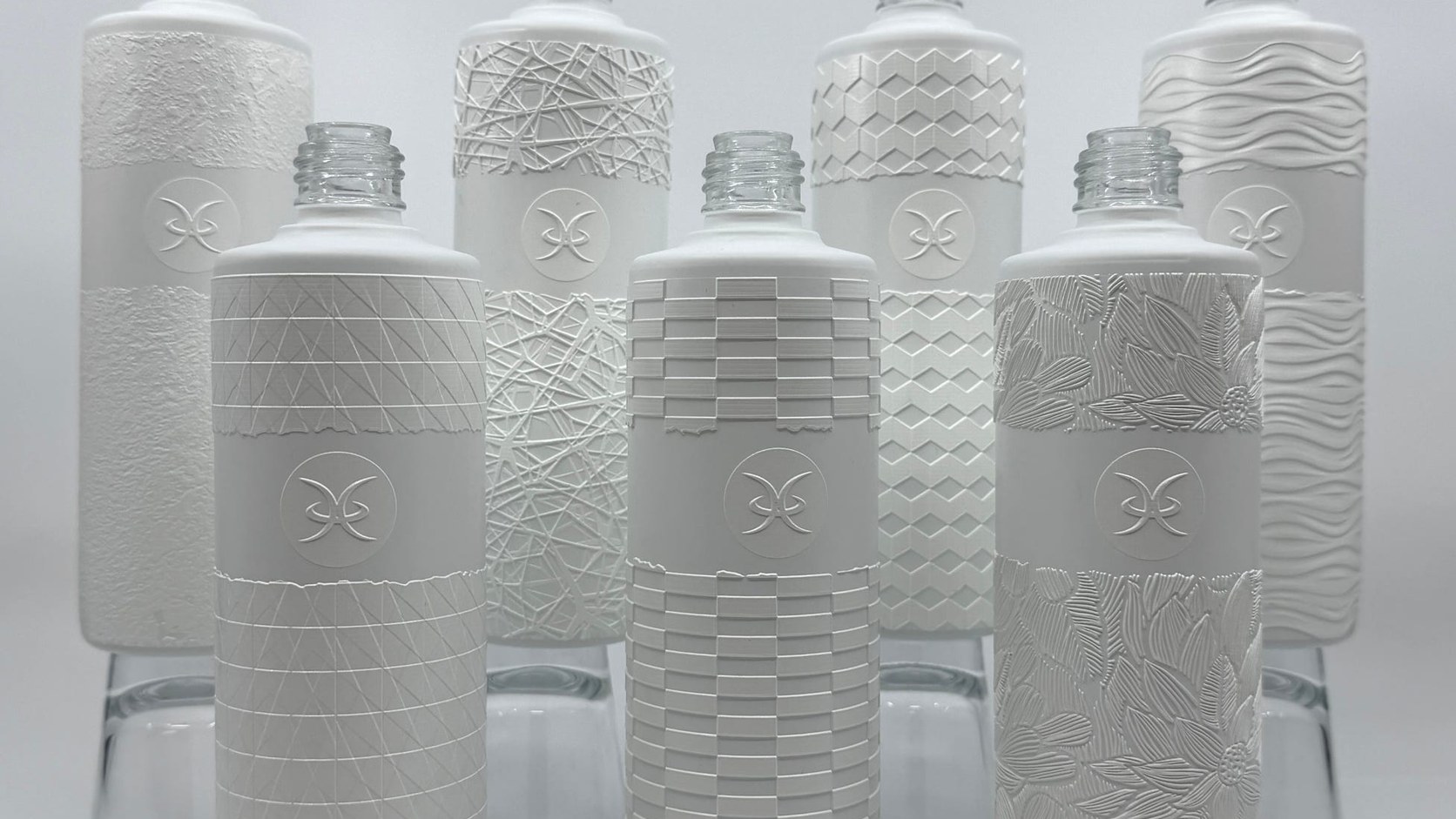 Seven clear glass bottles printed on the LSINC PeriQ360 with raised white tactile patterns, each bottle carrying a different texture