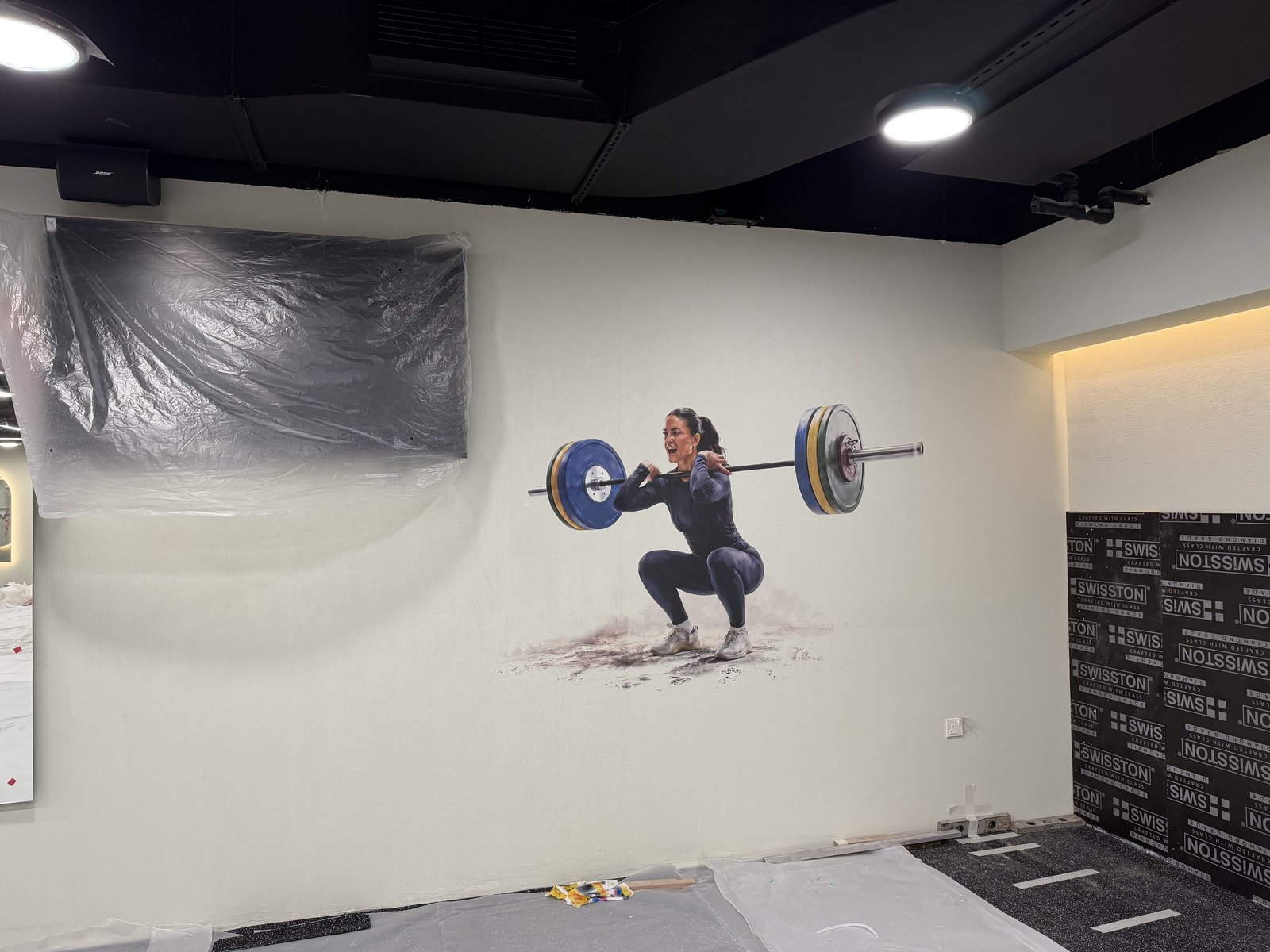 A weightlifter illustration printed directly onto a lightly textured gym wall, the surface texture visible through the image