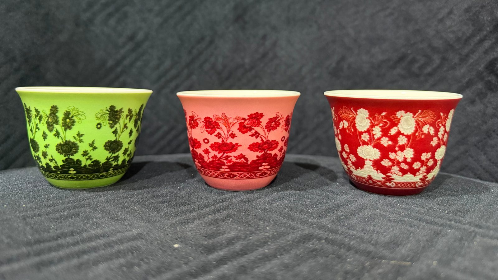 Three porcelain qahwa cups printed with one floral pattern in three colourways: black on green, red on pink and white on red