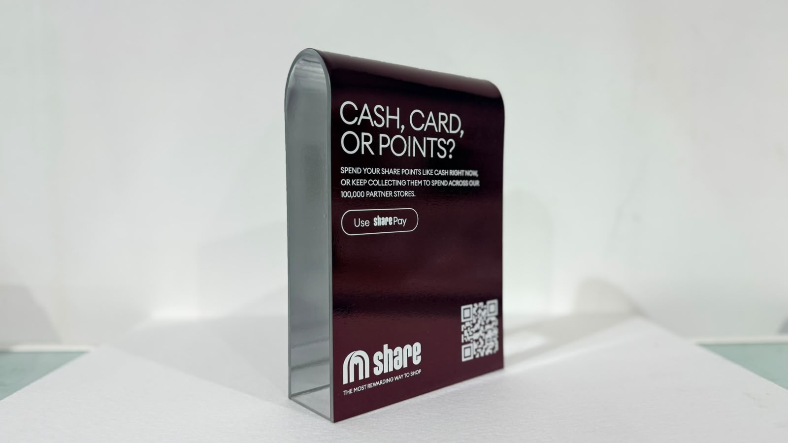 A share counter display from the side: a bent polished aluminium arch with a burgundy printed face and unprinted metal inside the curve