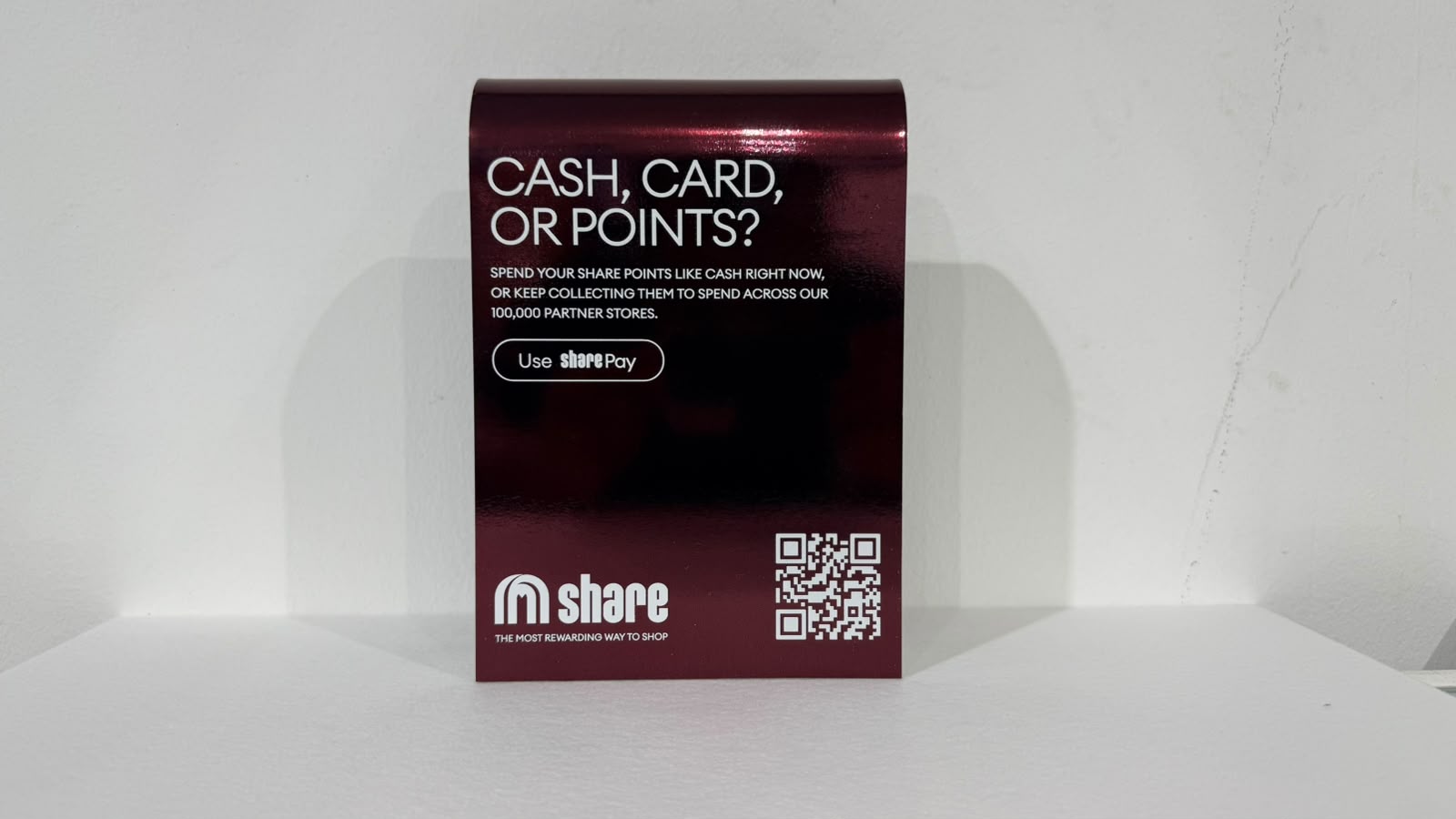 A share counter display in bent polished aluminium, printed in a see-through burgundy with white text and a QR code