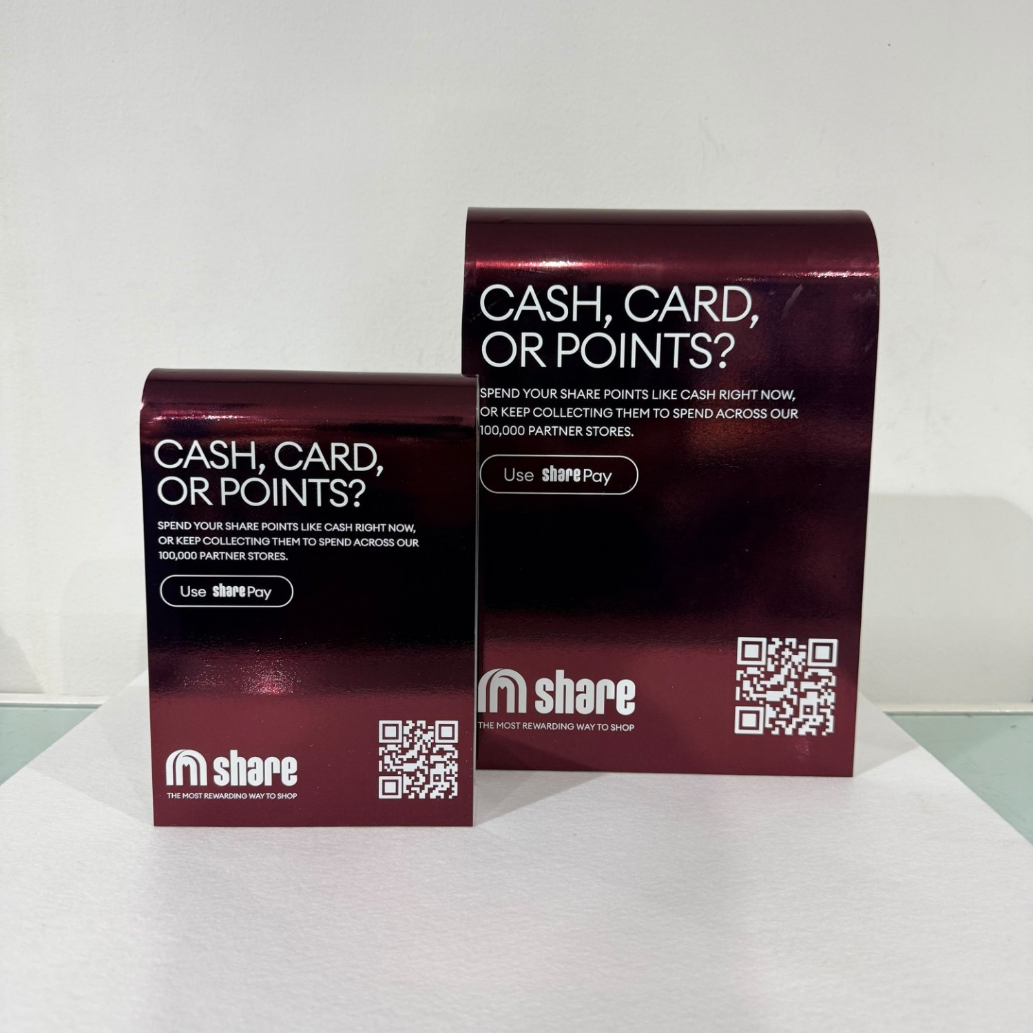 Two share counter displays in two sizes: polished aluminium bent into an arch, printed in a see-through burgundy with white lettering and a QR code