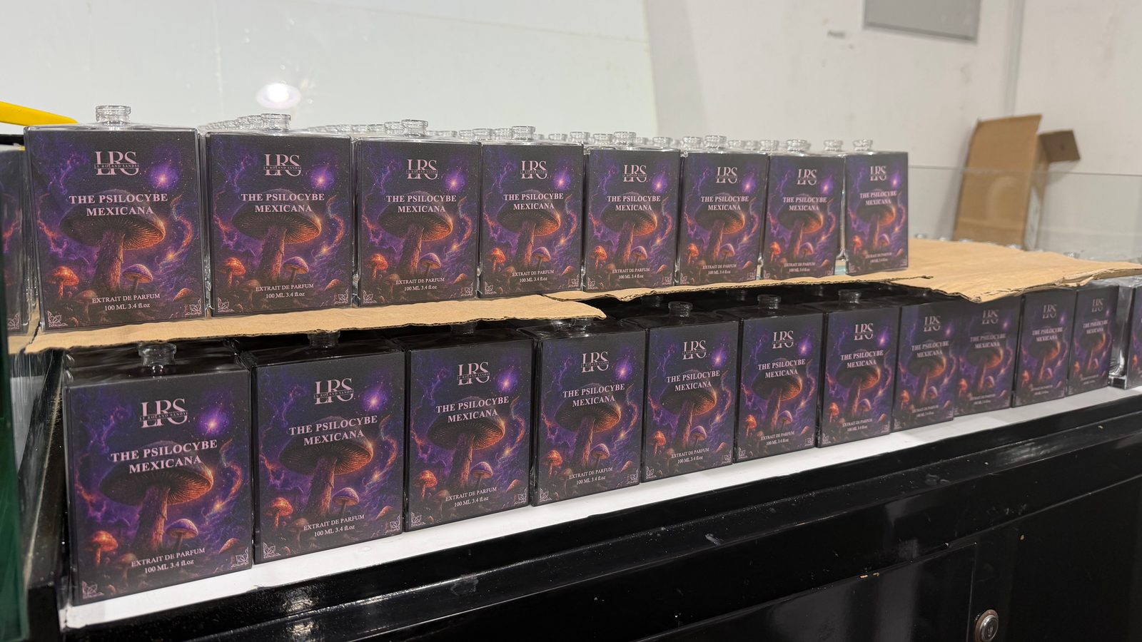 A run of square perfume bottles on a shelf, each printed across the front with purple mushroom artwork