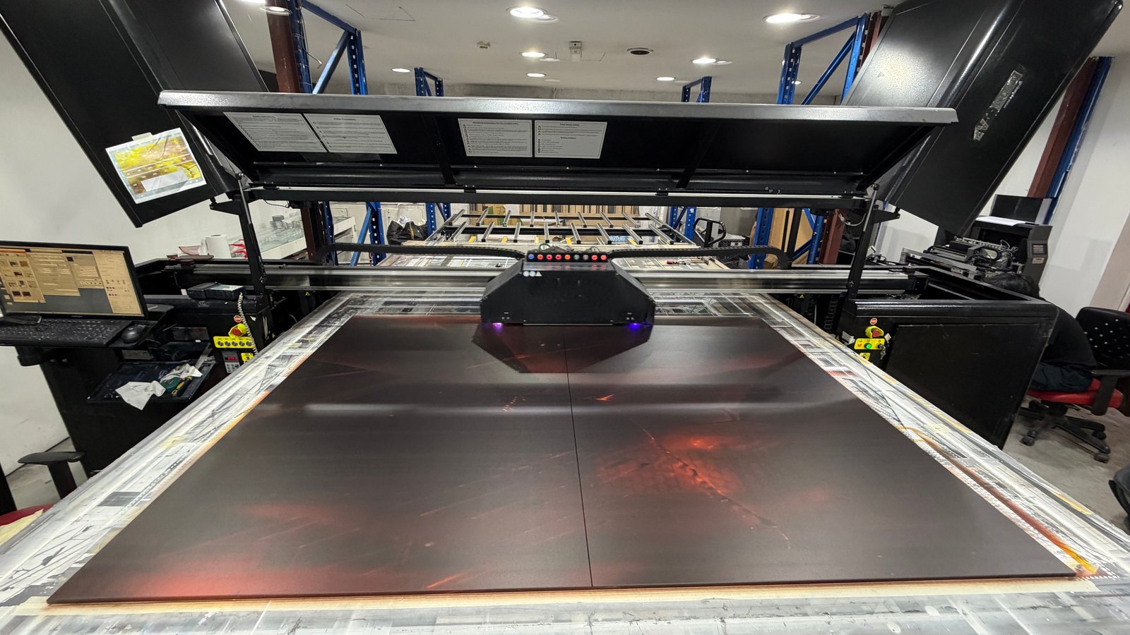 Two large glass panels lying side by side on the bed of the IQDEMY EVO 2500 flatbed press at Sun Studio in Dubai, with the print carriage on its gantry above them