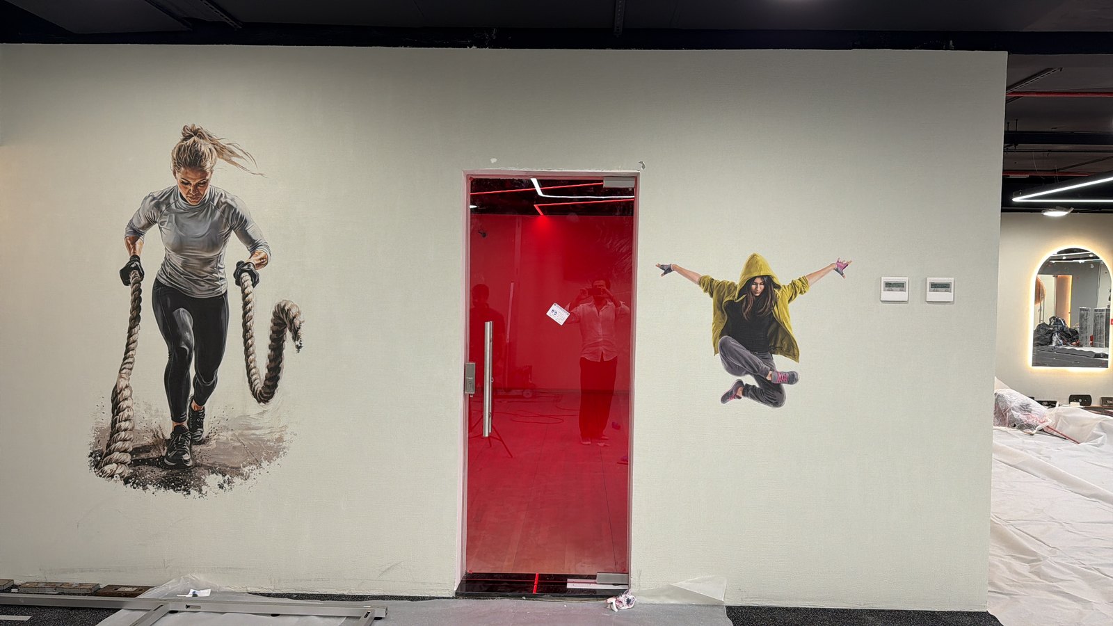 Two athlete illustrations printed directly onto a gym wall, one either side of a glass door, with no panel edge around either